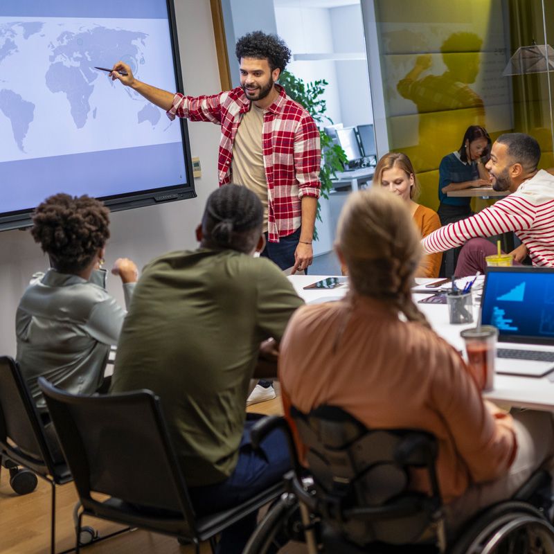 A presenter points at a screen displaying Spectrum Audio Visual's services to a team in Denver, CO.
