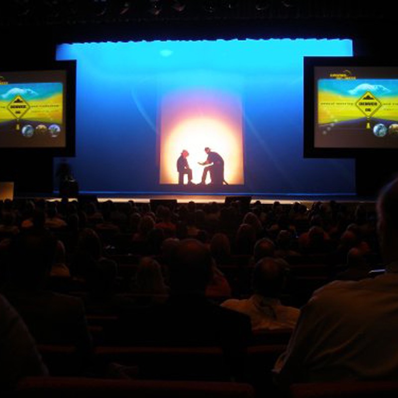 Backlit stage performers with a projector rental presentation slides on screen in Denver, CO